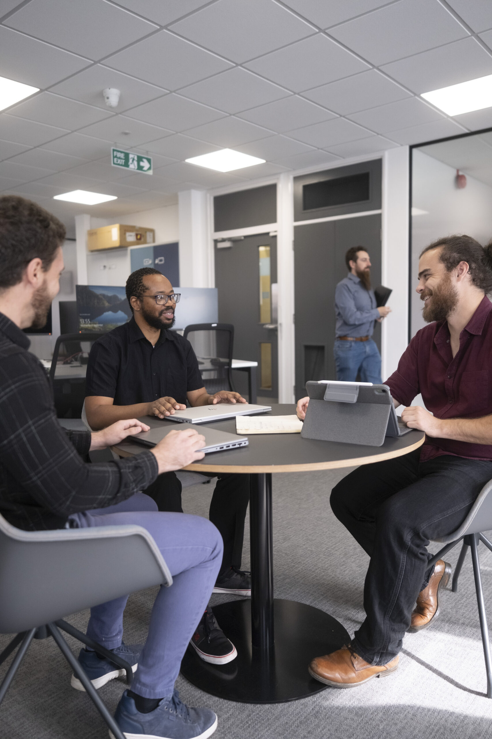 Three SE Labs experts are seated around a table, referring to paper documents and laptop computers