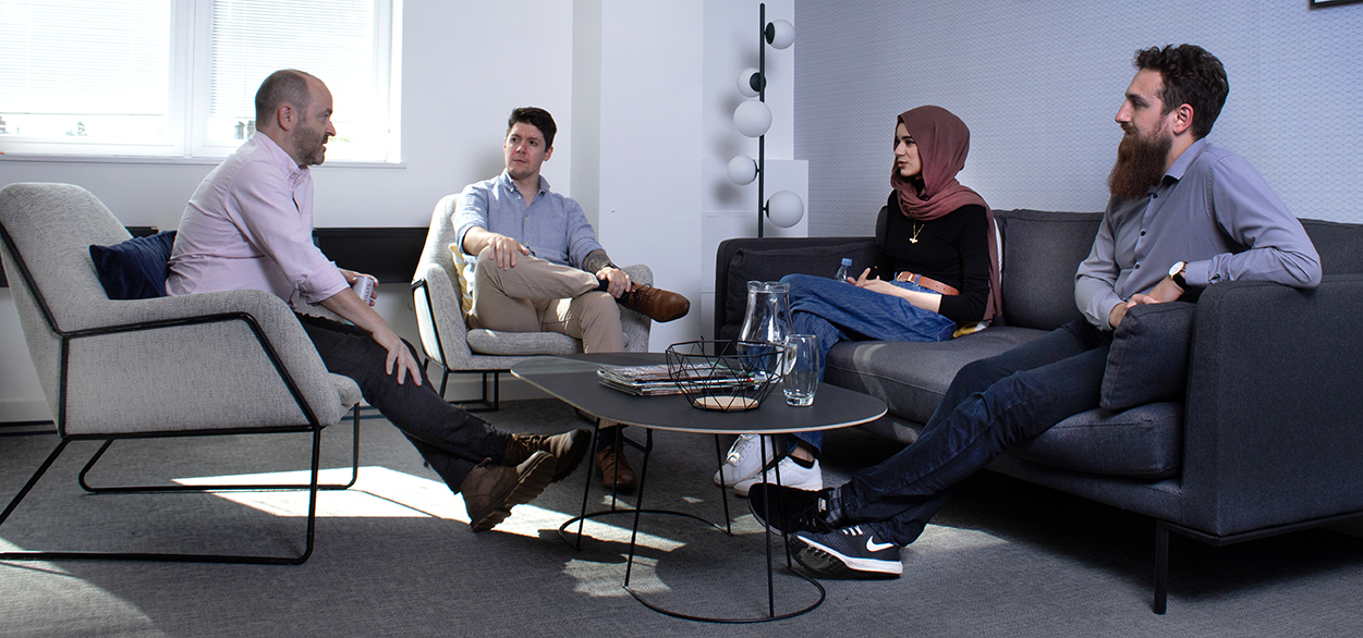 Four SE Labs employees sit around a low table on easy chairs and a sofa, deep in discussion
